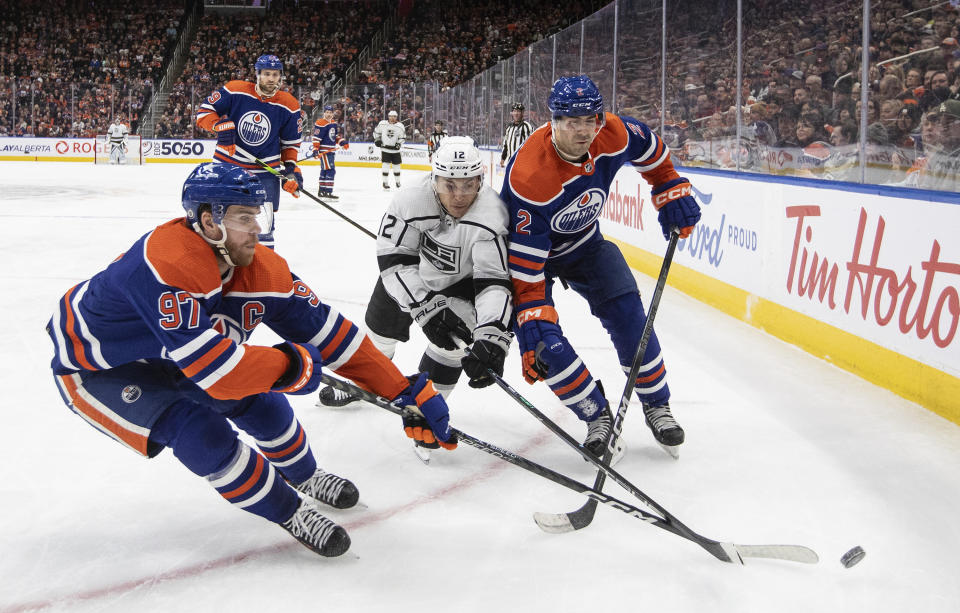 Los Angeles Kings' Trevor Moore (12) battles for the puck with Edmonton Oilers' Connor McDavid (97) and Evan Bouchard (2) during the third period of NHL hockey game in Edmonton, Alberta, on Monday, Feb. 26, 2024. (Jason Franson/The Canadian Press via AP)