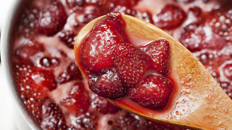 Strawberries on a wooden spoon and simmering in a pot below