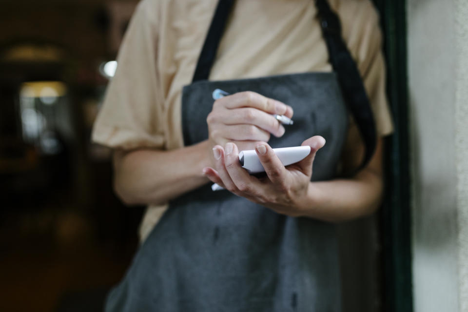 A waitress standing in the doorway of a restaurant and writing on her notepad