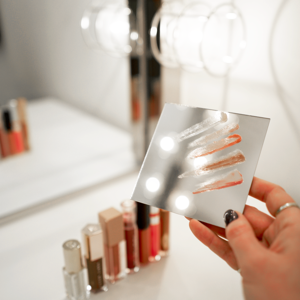 woman holding mirror with lip gloss swatches 