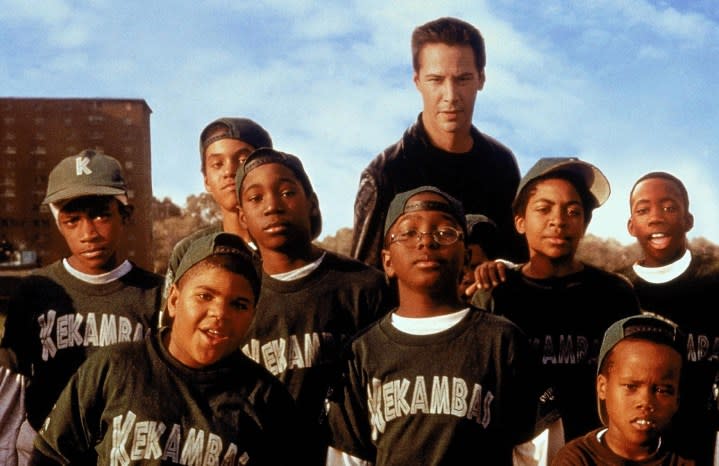 Keanu Reeves poses with a bunch of kids for a picture.