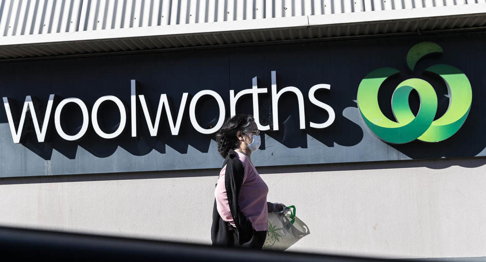 A woman walking past a Woolworths sign wearing a mask. 