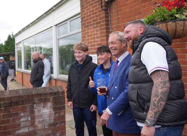 Nigel Farage poses for a photo with a man and two children, holding a pint