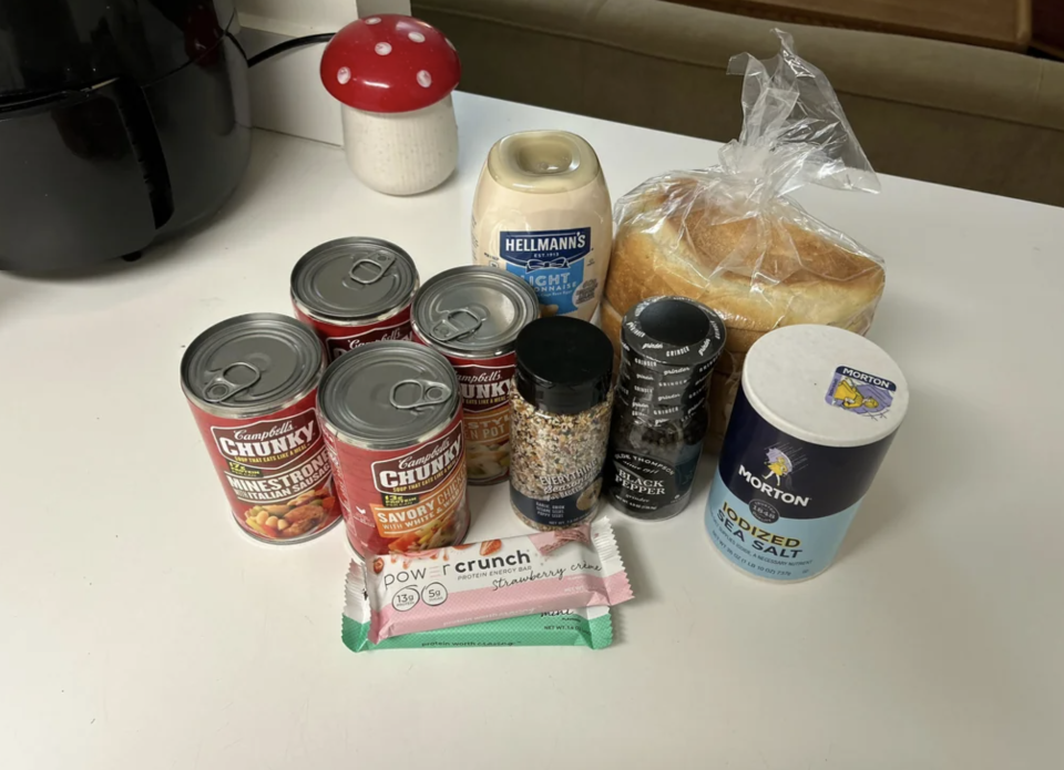 Various groceries on a counter, including Campbell's Chunky soup cans, bread, Hellmann's mayonnaise, Morton salt, spices, and a Power Crunch protein bar