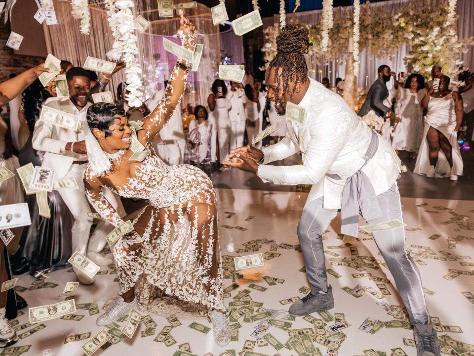 A bride and groom dance at their wedding as people throw money at them.