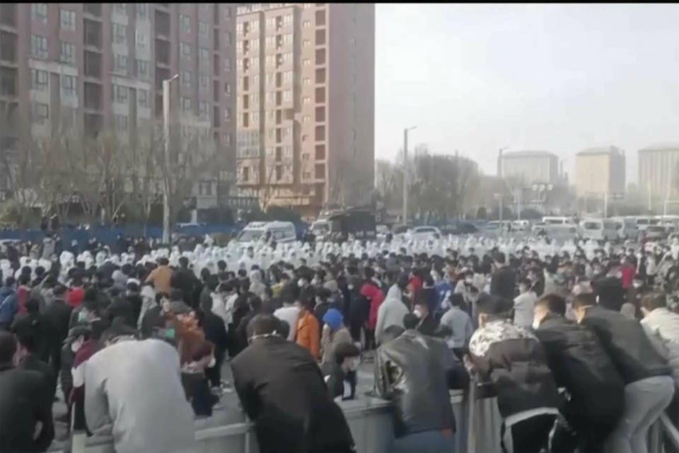 En esta fotografía suministrada el 23 de noviembre de 2022, manifestantes se enfrentan con personal de seguridad vestido de blanco en la fábrica operada por Foxconn Technology Group que incluye la planta de ensamble de iPhones más grande del mundo en Zhengzhou, en la provincia de Henan, en China. (AP)