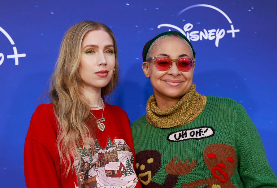Two people pose for the camera, one in a red sweater with a festive print, the other in a green sweater with cartoon figures