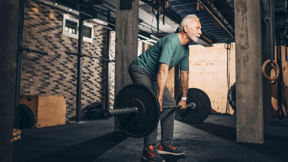 Senior man at gym doing a deadlift with heavy barbell