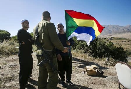 A member of the Druze community holds a Druze flag as he speaks to an Israeli soldier near the border fence between Syria and the Israeli-occupied Golan Heights, near Majdal Shams June 18, 2015. REUTERS/Baz Ratner