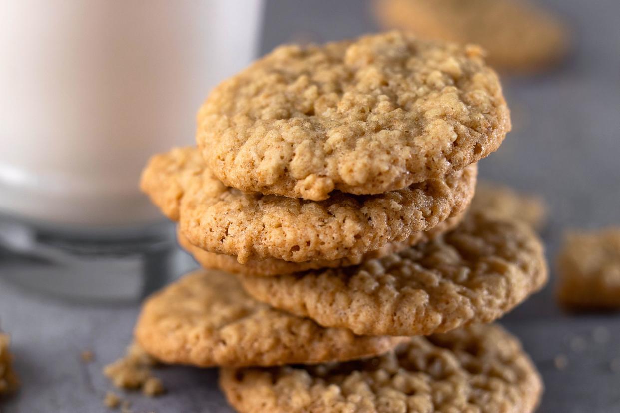 Stack of five oatmeal cookies with a blurred background of a glass of milk and oatmeal cookies on a grey wooden table