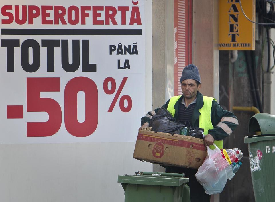 A municipal worker carries garbage in Bucharest, Romania, back dropped by a shop window advertising price reductions for sports equipment, Monday, March 19, 2012. The coldest winter in living memory is over, and spring has arrived in Prague, Belgrade and Bucharest, but from the look in shop windows, with massive reductions and bargains galore, you'd think we were still in the winter sales. (AP Photo/Vadim Ghirda)