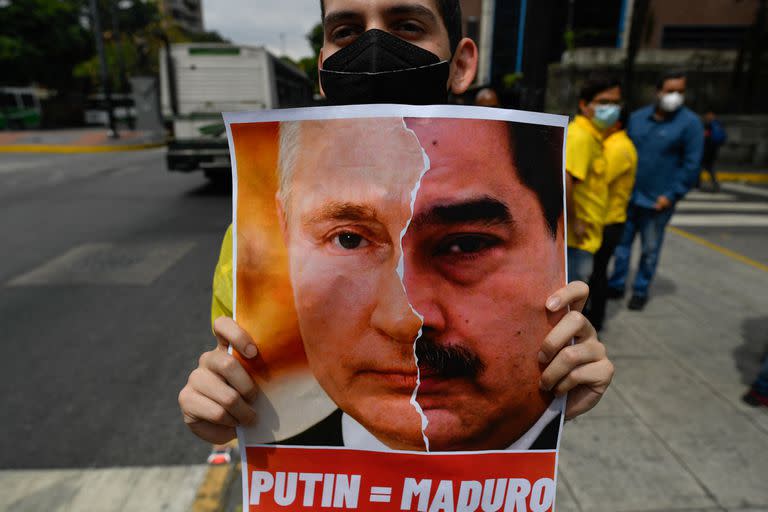 Un activista miembro del partido opositor Primero Justicia sostiene una pancarta con el rostro del presidente ruso Vladimir Putin y el presidente venezolano Nicolás Maduro durante una protesta contra la invasión rusa en Ucrania, en Caracas el 4 de marzo de 2022. 