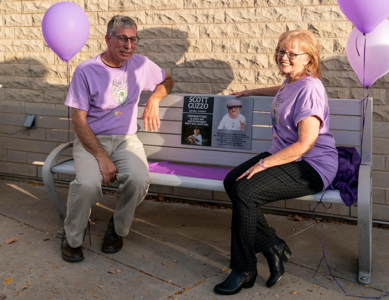 Bob and Paula Guzzo sit on the bench dedicated to their late son Scott Guzzo for the first time outside the Ford Center during a ceremony Thursday, Oct. 25, 2023. Scott Guzzo was diagnosed with Crane-Heise syndrome, a rare craniofacial condition, at age 10. He was an advocate for the disabled and beloved community member who died in June at age 39.