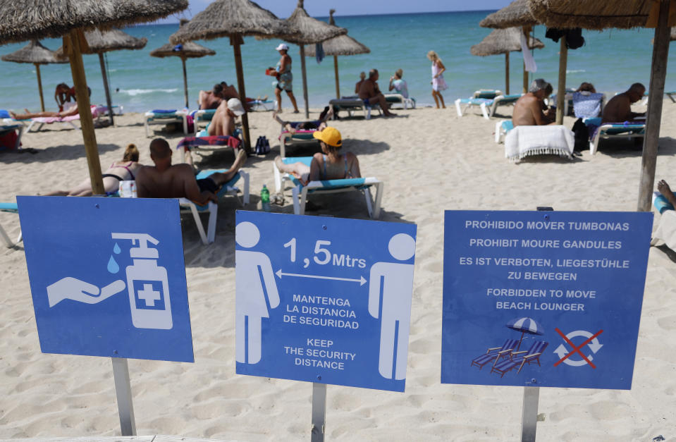 15 August 2020, Spain, Palma: People sunbathe and swim on the beach of Arenal in Mallorca. In the foreground you can see a sign indicating the distance regulations. In view of the increased risk of infection, the German government has classified almost all of Spain, including Majorca, as a risk area. The classification means that returning holidaymakers are required to test for the coronavirus. Photo: Clara Margais/dpa (Photo by Clara Margais/picture alliance via Getty Images)