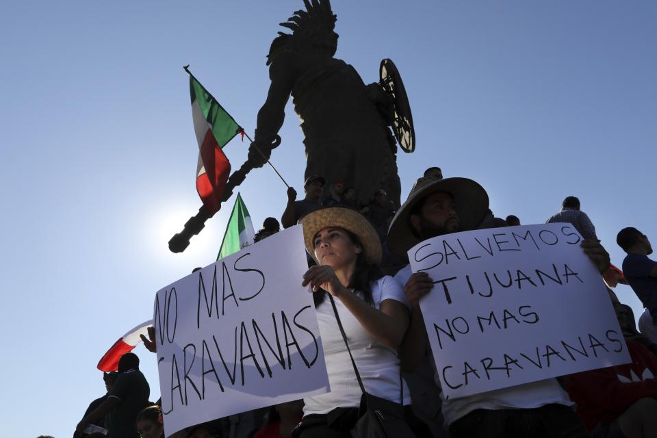 Manifestantes sostienen carteles bajo la estatua del emperador azteca Cuauhtémoc como protesta contra los miles de migrantes centroamericanos que han llegado a la ciudad en Tijuana, México, el domingo 18 de noviembre de 2018. (AP Foto/Rodrigo Abd)