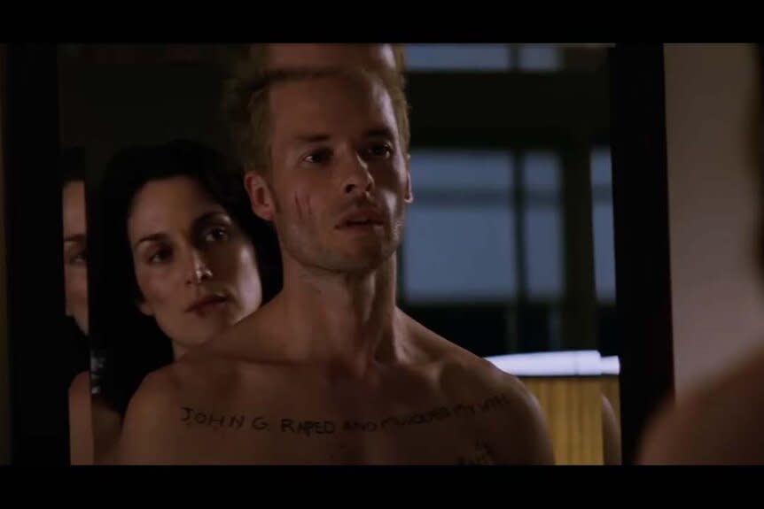 Natalie (Carrie-Anne Moss) stands behind Leonard Shelby (Guy Pearce) in a mirror in Memento (2000).