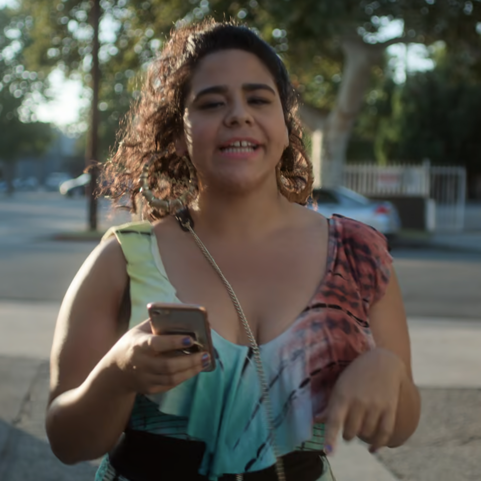 Jasmine walking on a street, holding a smartphone, wearing a sleeveless top