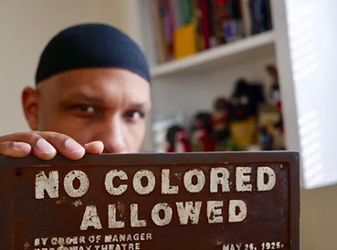 Black History 101 Mobile Museum founder Khalid el-Hakim holds up a "No Colored Allowed" sign in 2022.