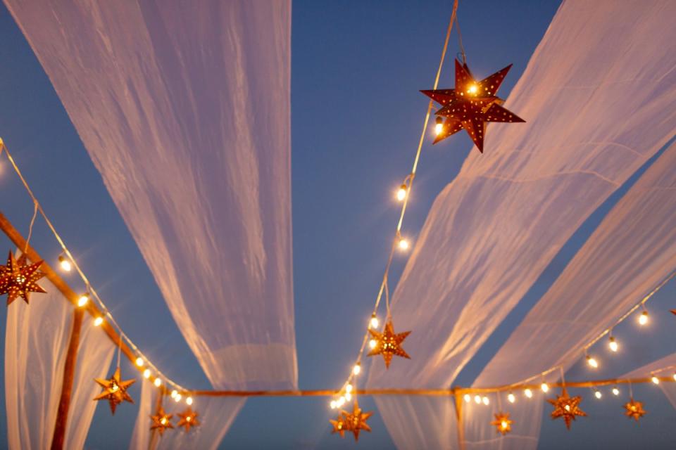 Star lanterns hang with string lights in the evening sky with drapery.