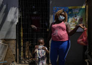 Chilean-born Moises holds the Chilean, government-issued identification card of his dad Edanold Delva, next to his mother Jaqueline Michel, who also has permanent residency, outside their home in the Bosque Hermoso camp settled by migrants in Lampa, Chile, Friday, Oct. 1, 2021. Despite having a permanent residency visa, she says that in Immigration they ask for “a bank certificate and a proof of residence” which she cannot get because she lives in an illegal land occupation. (AP Photo/Esteban Felix)