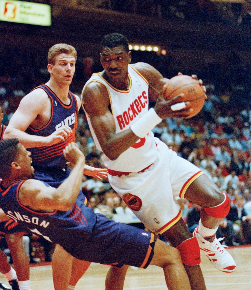 Houston Rockets Hakeem Olajuwon, right, drives to the basket as Phoenix Suns Kevin Johnson falls backwards and Joe Kleine  looks on during the first quarter of their NBA Playoff game, Sunday, May 8, 1994, Houston, Tex. 