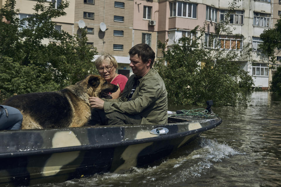 Residentes y su perro son evacuados en un bote de un vecindario inundado en Jersón, Ucrania, el jueves 8 de junio de 2023. (AP Foto/Libkos)