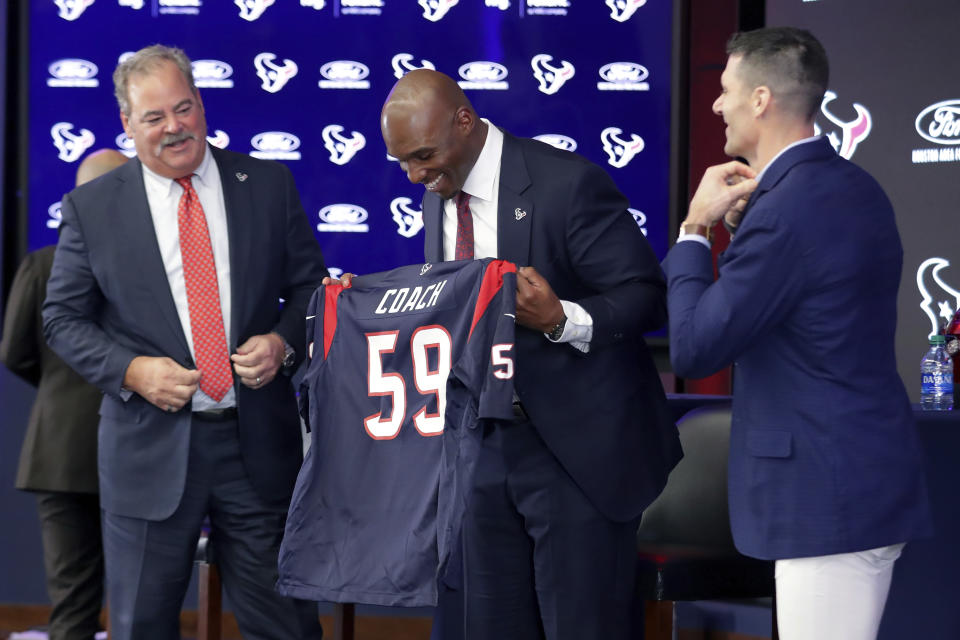 El recién contratado entrenador en jefe de los Texans, DeMeco Ryans (centro), recibe una camiseta por parte del propietario del equipo Cal McNair (izquierda) y del gerente general Nick Caserio durante una conferencia de prensa para presentar a Ryans como entrenador, en el NRG Stadium, el jueves 2 de febrero de 2023. (AP Foto/Michael Wyke)