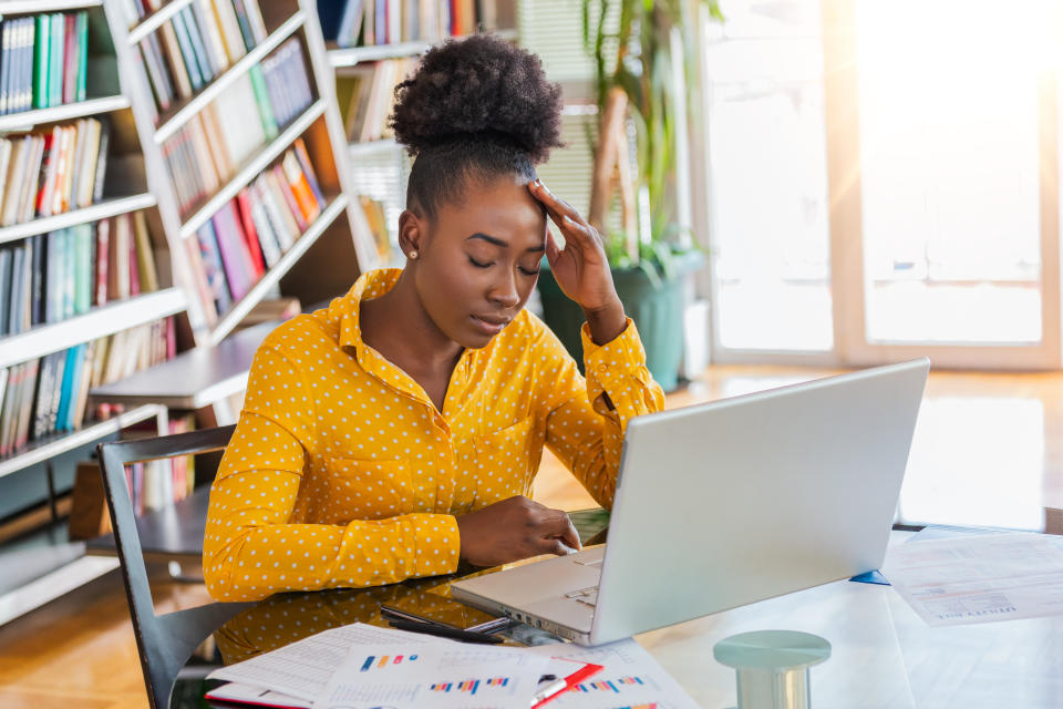 Young frustrated woman working at office desk in front of laptop suffering from chronic daily headaches, treatment online, appointing to a medical consultation, electromagnetic radiation, sick pay