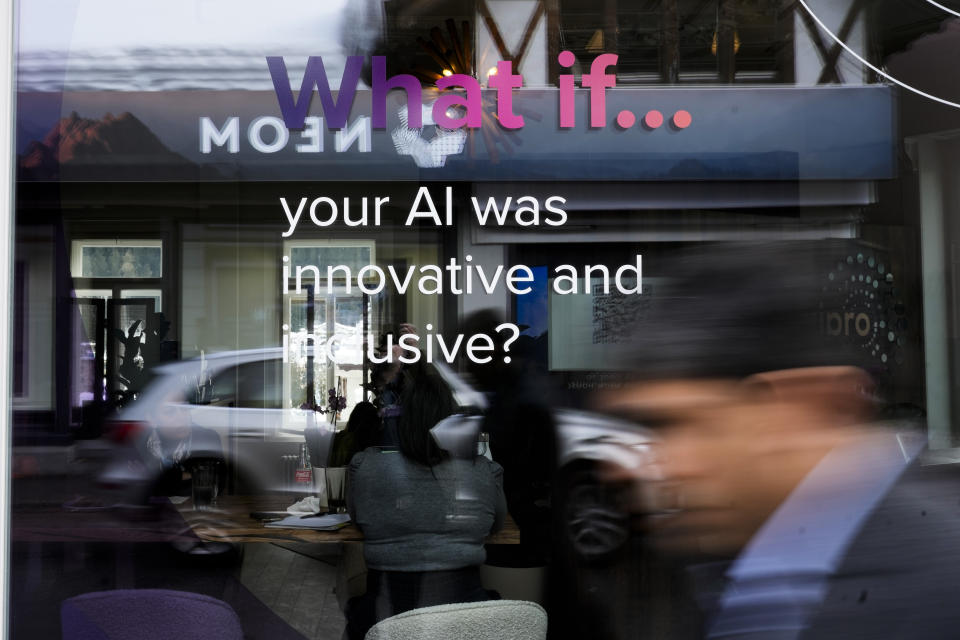 People reflected in a window of a building at the Davos Promenade with a slogan about AI alongside the World Economic Forum in Davos, Switzerland, Thursday, Jan. 18, 2024. The AI technology has taken a large and growing slice of attention in Davos, this year the theme of Artificial Intelligence "as a driving force for the economy and society" will get about 30 separate sessions. (AP Photo/Markus Schreiber)