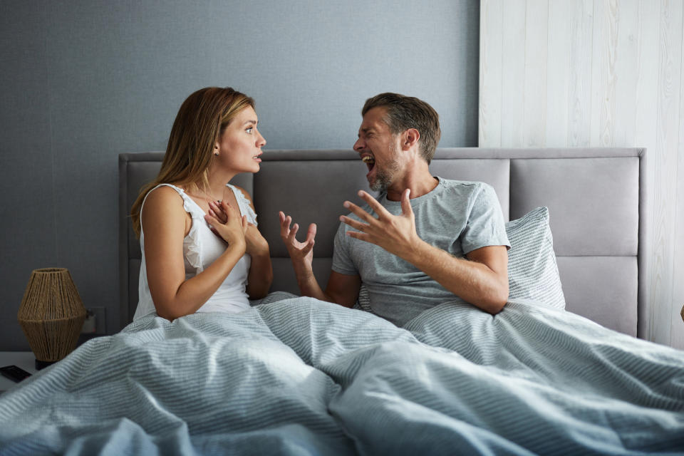 A couple in bed engaged in an intense conversation with expressive hand gestures