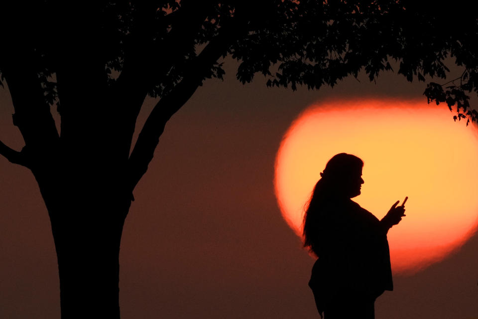 FILE - A woman looks at her phone while watching the sun set as triple-digit heat indexes continue in the Midwest Sunday, Aug. 20, 2023, in Kansas City, Mo. A number of Americans on Thursday, Feb. 22, 204, are dealing with cellular outages on AT&T, Cricket Wireless, Verizon, T-Mobile and other service providers, according to data from Downdetector. AT&T, who was the hardest hit, is actively working to restore service to all of its customers. (AP Photo/Charlie Riedel, File)