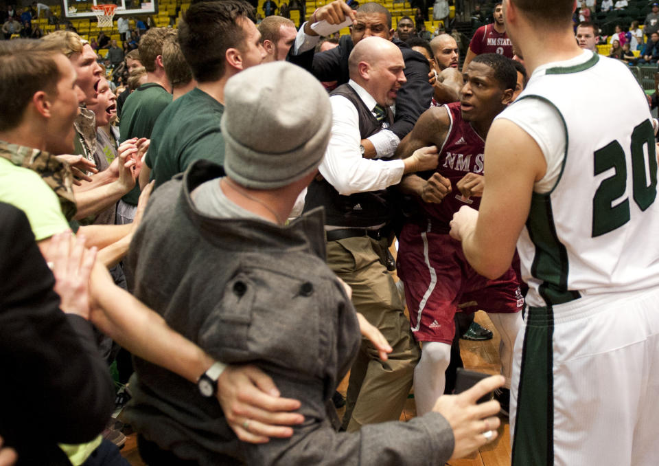 In this Thursday, Feb. 27, 2014 photo, New Mexico State's DK Eldridge, at right center in red and white uniform, is controlled by security during a brawl involving players and fans who came onto the court when New Mexico State guard K.C. Ross-Miller hurled the ball at Utah Valley's Holton Hunsaker seconds after the Wolverines' 66-61 overtime victory against the Aggies in Orem, Utah. (AP Photo/The Daily Herald, Grant Hindsley) MANDATORY CREDIT