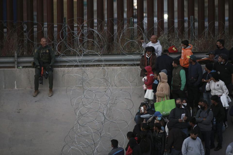 Migrants stand behind barbed wire as a barrier from crossing into El Paso, Texas.