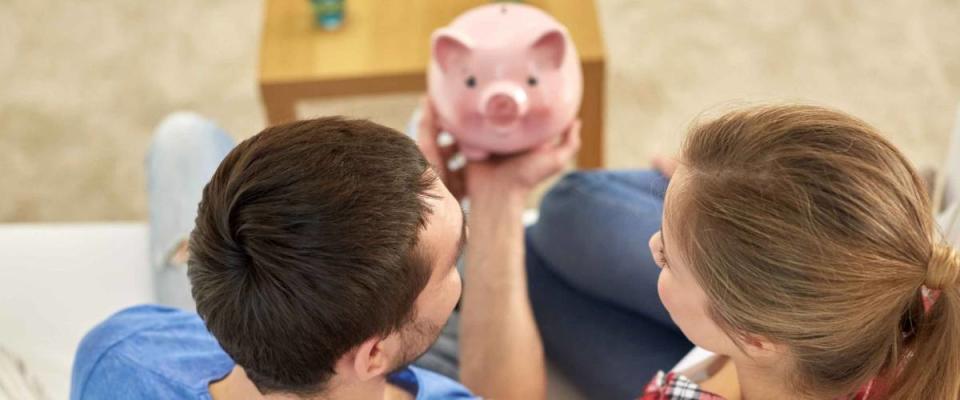 money, home, finance and relationships concept - close up of couple with piggy bank sitting on sofa