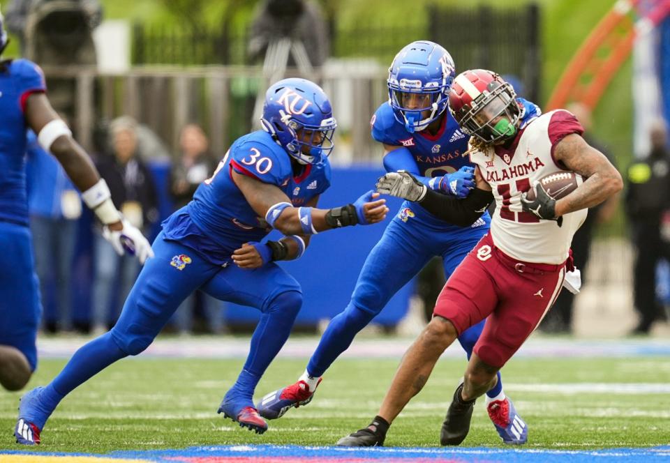 Oklahoma wide receiver Jadon Haselwood (11) is tackled by Kansas cornerback Jeremy Webb (9) and linebacker Rich Miller (30) on Oct. 23, 2021.