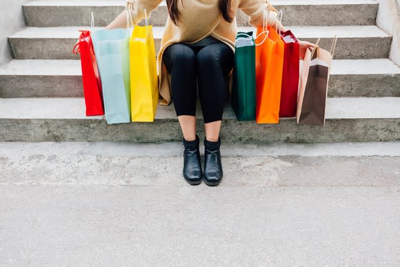 A woman sitting on stairs with different color bags on both sides of her.