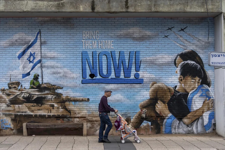 People walk past a graffiti calling for the return of the hostages kidnapped during the Oct. 7 Hamas cross-border attack in Israel, in Kfar Saba, Israel, Monday, Feb. 26, 2024. (AP Photo/Ohad Zwigenberg)