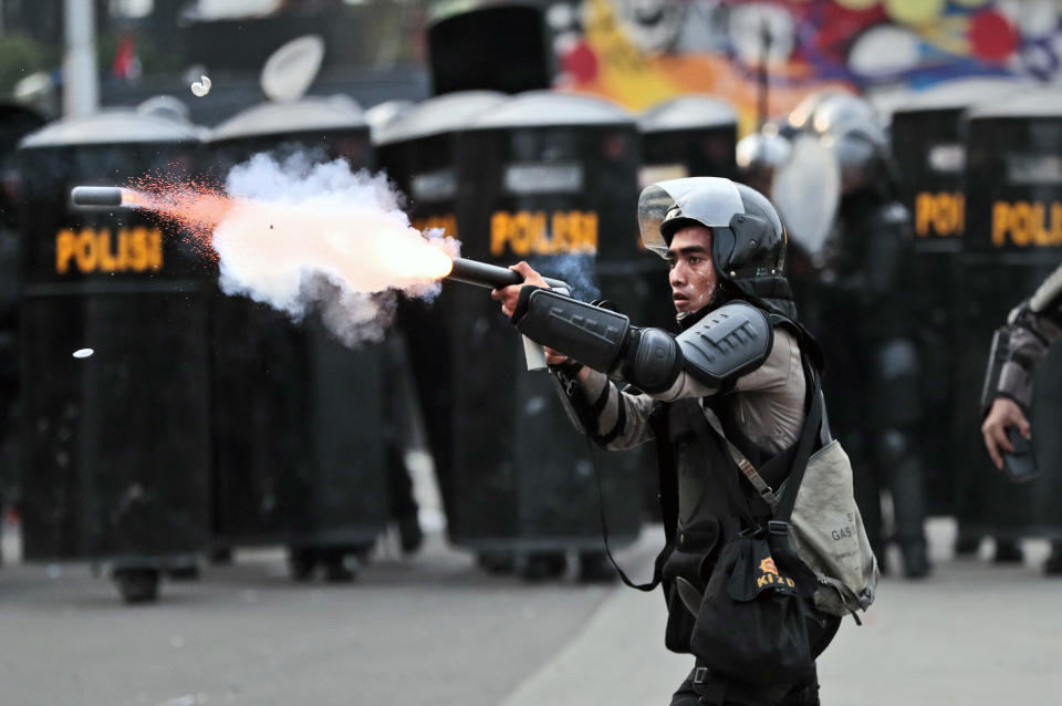 A police officer fires a projectile towards protesters during a rally against a controversial bill on job creation in Jakarta, Indonesia, Thursday, Oct. 8, 2020. Thousands of enraged students and workers staged rallies across Indonesia on Thursday in opposition to the new law they say will cripple labor rights and harm the environment. (AP Photo/Dita Alangkara)