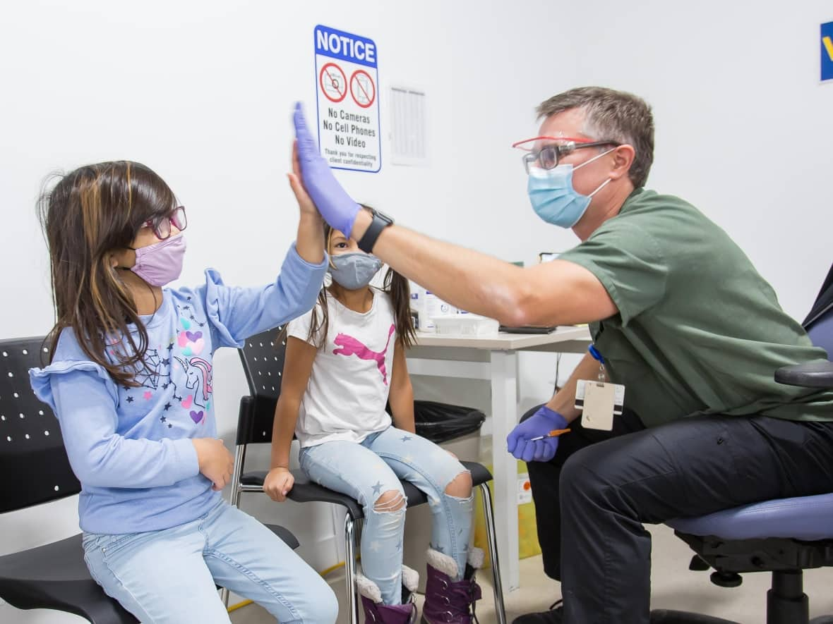 Sisters Raya, 7, left, and Sky, 5, middle, are shown getting a first dose of the pediatric Pfizer vaccine at the Boardwalk Vaccination Clinic in Waterloo, Ont. on Nov. 26, 2021.  (Submitted by Region of Waterloo Public Health - image credit)