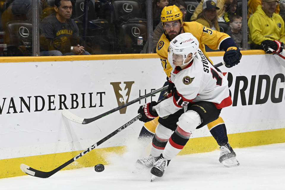 Ottawa Senators left wing Tim Stützle (18) tries to get control of the puck as Nashville Predators defenseman Dante Fabbro (57) defends during the first period of an NHL hockey game Saturday, Dec. 10, 2022, in Nashville, Tenn. (AP Photo/Mark Zaleski)