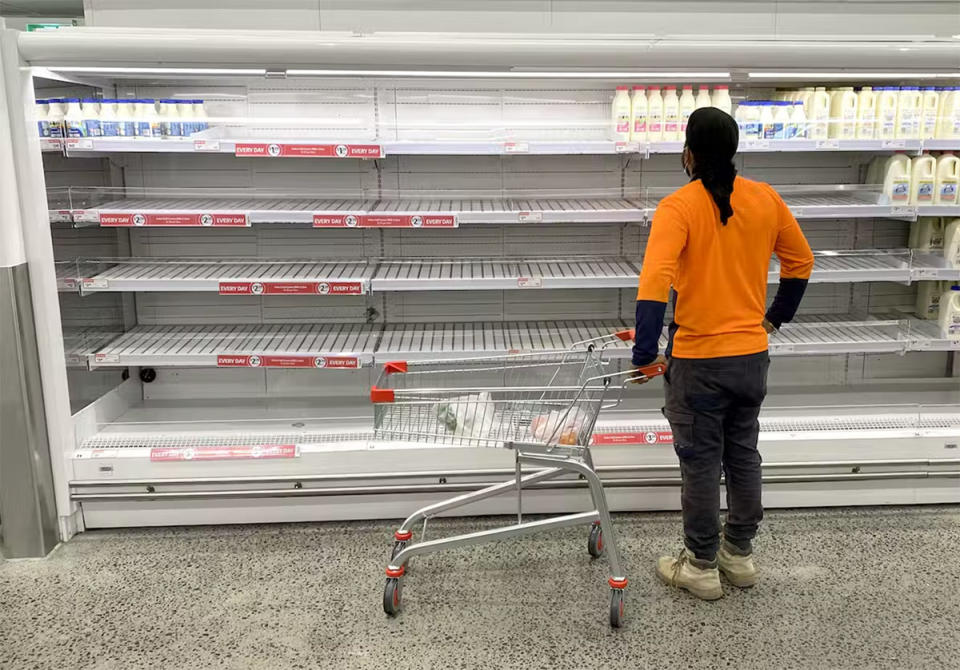 Coles supermarket shopper in front of mostly empty milk shelves
