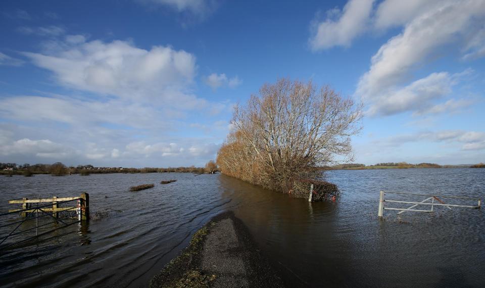 In this photo taken Sunday Feb. 2, 2014, floodwater from the River Parrett blocks a road from Thorney to Barrington in Somerset, England. Here on the Somerset Levels _ a flat, marshy region of farmland dotted with villages and scored by rivers and ditches _ it's often wet. But not this wet. Thousands of acres of this corner of southwest England have been under water for weeks, some villages have been cut off for more than a month, and local people forced to take boats to get to school, work and shops are frustrated and angry. Some blame government budget cuts and environmental bureaucracy. Others point to climate change. Even plump, endangered water voles are the target of ire. (AP Photo/Alastair Grant)