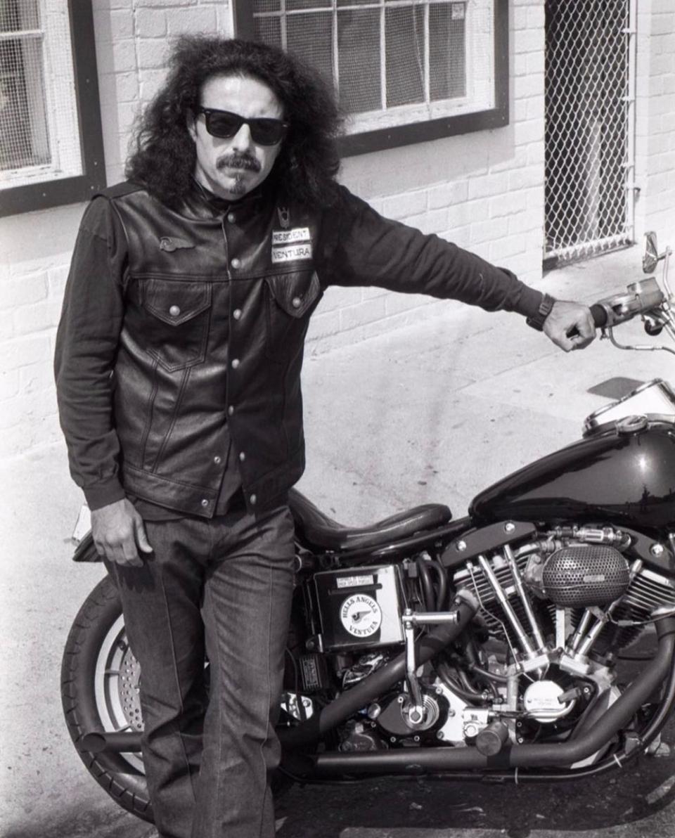 A black and white photo of George Christie standing next to his motorcycle