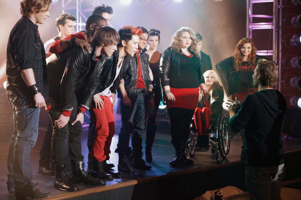 The cast of "The Glee Project" season two in black-and-red costumes talking to choreographer Zach Woodlee.