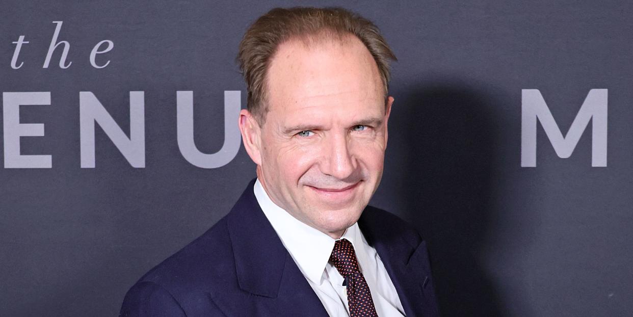 ralph fiennes wearing a white shirt burgundy tie and navy suit jacket posing for a picture at the premiere of his film the menu in 2022