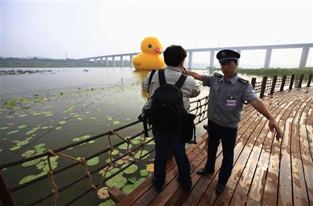 A security guard tries to ask a photographer to leave as he takes pictures of an inflated Rubber Duck by Dutch conceptual artist Florentijn Hofman floating on a lake at the 9th China International Garden Expo in Beijing, September 6, 2013. REUTERS/Petar Kujundzic