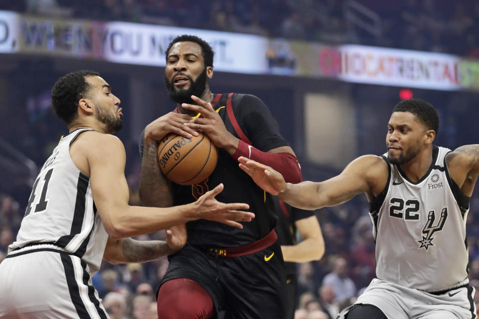 Cleveland Cavaliers' Andre Drummond, center, drives between San Antonio Spurs' Trey Lyles, left, and Rudy Gay, right, in the first half of an NBA basketball game, Sunday, March 8, 2020, in Cleveland. (AP Photo/Tony Dejak)