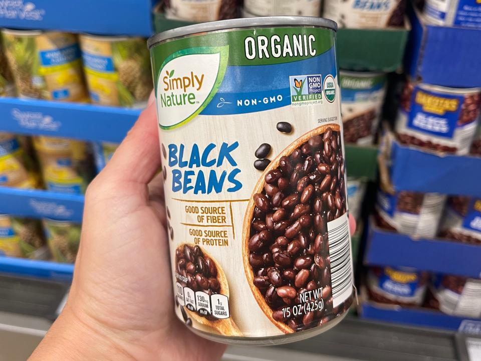 A hand holding a can of Simply Nature organic black beans.