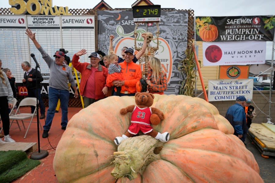 Travis Gienger of Anoka, Minn., holds his two-year-old daughter Lily and poses behind his pumpkin called “Michael Jordan” after winning the Safeway 50th annual World Championship Pumpkin Weigh-Off in Half Moon Bay, Calif., Monday, Oct. 9, 2023. Gienger won the event with a pumpkin weighing 2749 pounds. (AP Photo/Eric Risberg)
