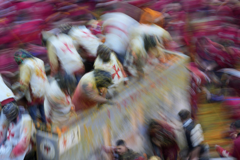 People wearing protection helmets and costumes pelt each other with oranges during the 'Battle of the Oranges" part of Carnival celebrations in the northern Italian Piedmont town of Ivrea, Italy, Tuesday, Feb. 13, 2024. (AP Photo/Antonio Calanni)